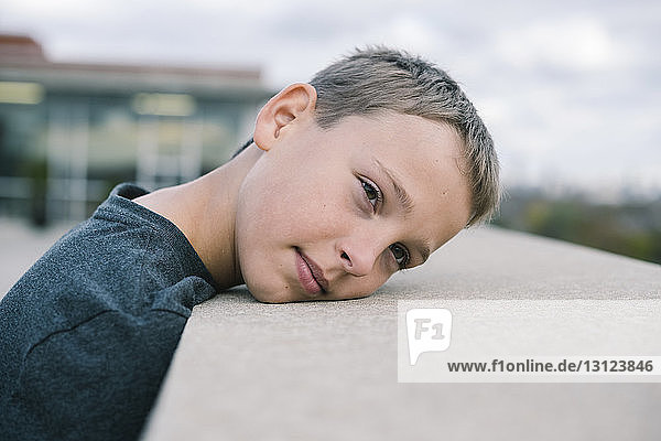 Close-up of thoughtful boy looking away while leaning on retaining wall against sky