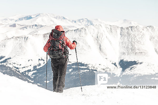 Rückansicht einer Wanderin mit Rucksack  die Wanderstöcke hält  während sie vor schneebedeckten Bergen steht