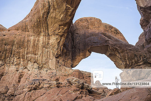 Low angle view of woman standing at rock formation against sky
