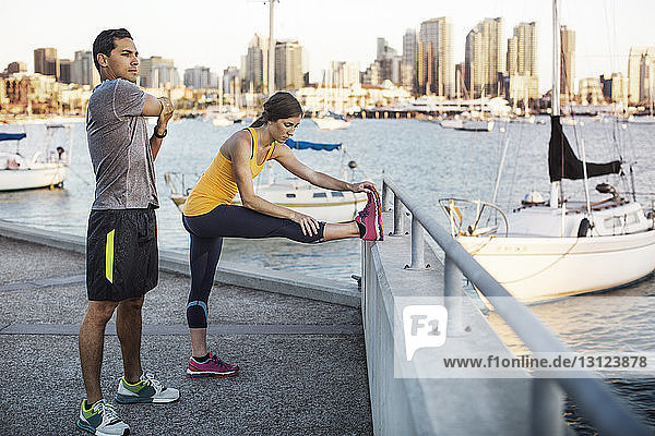 Male and female athletes doing stretching exercises on pier by harbor