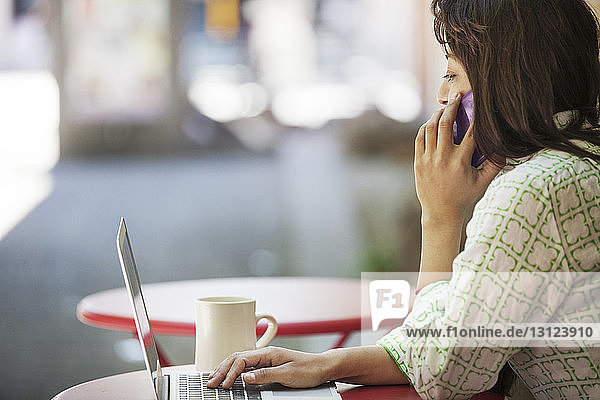 Seitenansicht einer Frau mit Laptop und Smartphone im Straßencafé