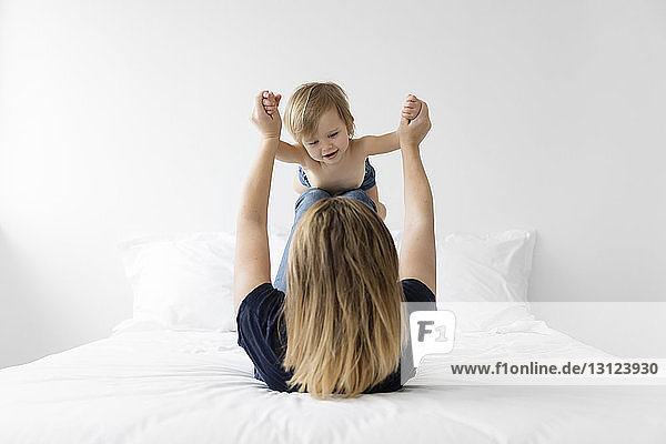 Rear view of mother playing with shirtless daughter while lying on bed at home