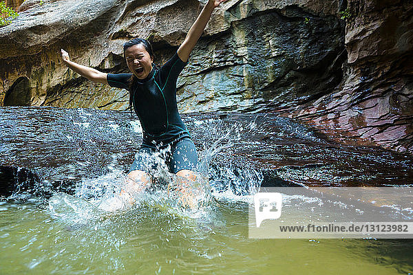 Fröhliche Frau springt in Teich von Felsformation