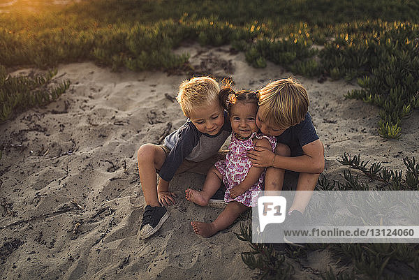 High angle view of siblings sitting on sand at beach during sunset
