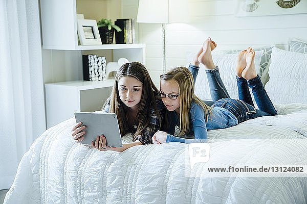 Sisters using tablet computer while lying on bed at home