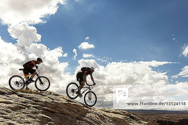 Seitenansicht von Mountainbikern auf Fahrrädern vor bewölktem Himmel