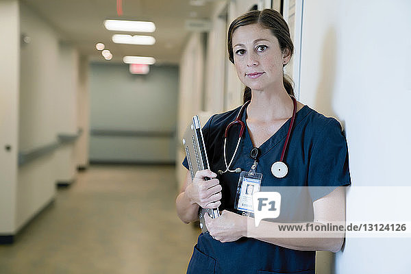 Portrait of confident female doctor holding laptop computer while standing in hospital lobby