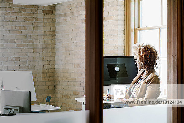 Geschäftsfrau  die in einem kreativen Büro arbeitet  durch eine Glaswand gesehen