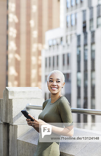 Lächelnde Geschäftsfrau benutzt Mobiltelefon auf Bürobalkon