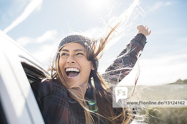 Fröhliche junge Frau genießt im Auto gegen den Himmel