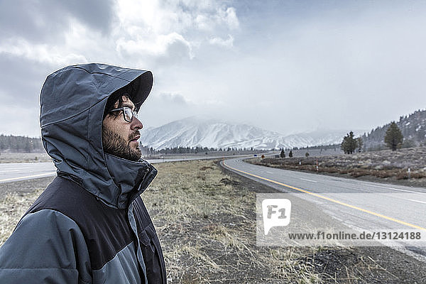 Side view of man wearing hooded jacket while standing on field against Mammoth Mountain