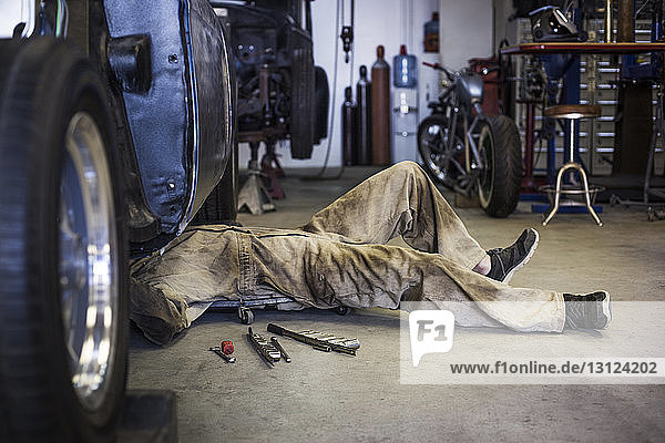 Seitenansicht eines Mechanikers auf einem Kriechwagen bei der Arbeit unter dem Auto in einer Autowerkstatt