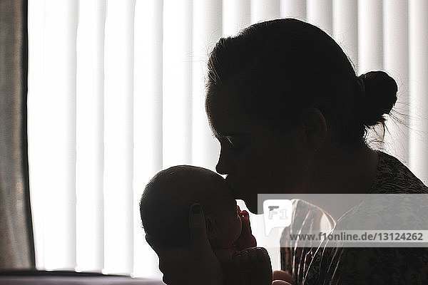 Mutter küsst neugeborene Tochter  während sie zu Hause sitzt