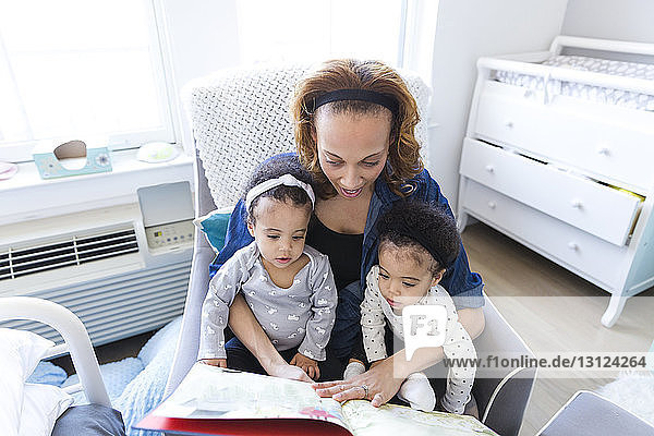 Schrägansicht der Mutter beim Lesen eines Märchenbuchs für Töchter zu Hause