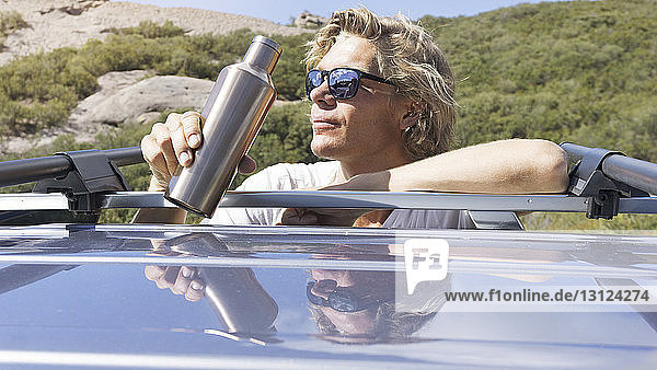 Man in sunglasses drinking water while leaning on car