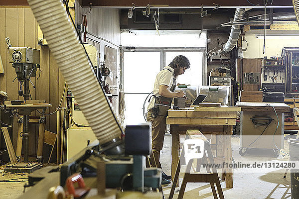 Side view of carpenter examining wooden plank at workbench in workshop