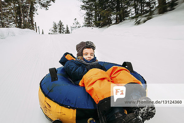 Boy tobogganing with tube sled on snow covered field