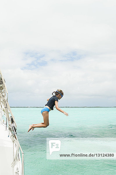 Side view of girl diving in sea against cloudy sky