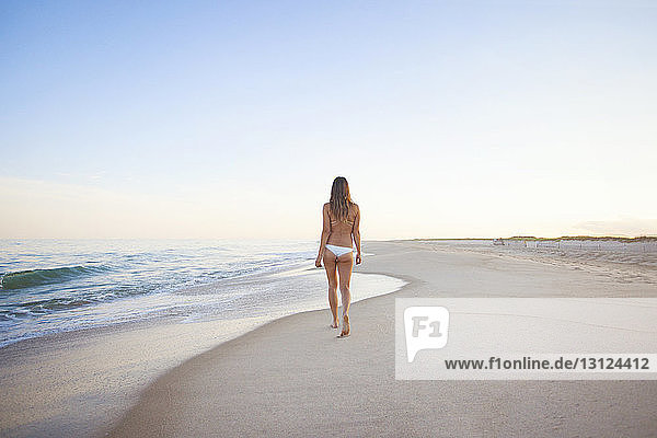 Rückansicht einer Frau  die bei klarem Himmel am Strand spazieren geht