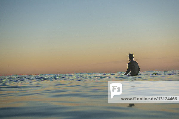 Mittlerer Abstand eines männlichen Surfer im Meer gegen klaren Himmel bei Sonnenuntergang