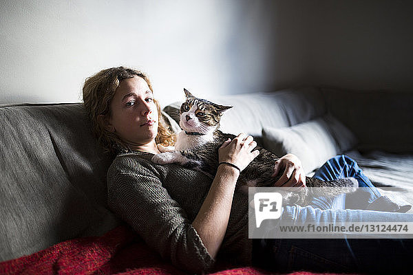 Porträt einer Frau mit Katze  die sich zu Hause auf dem Sofa ausruht