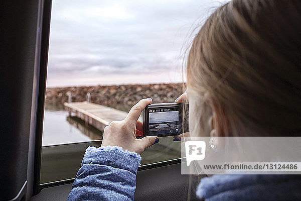 Close-up of girl photographing lake through window