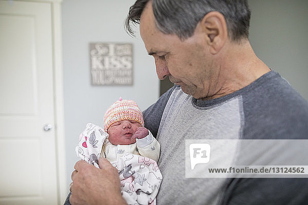 Großvater trägt neugeborene Enkelin  während er zu Hause steht