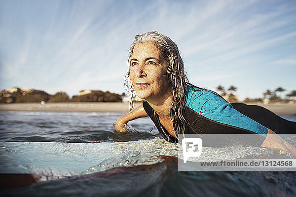 Reife Frau schaut beim Surfen auf See weg