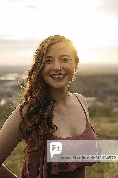 Porträt einer fröhlichen jungen Frau  die bei Sonnenuntergang auf dem Feld steht