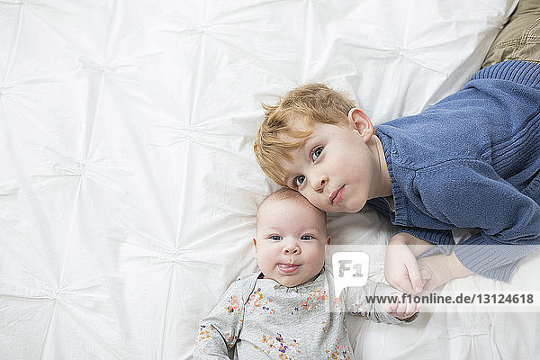 Overhead portrait of cute siblings lying on bed at home