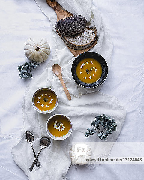 Draufsicht auf die in Schüsseln servierte Suppe mit Kürbissen und Broten auf Textil