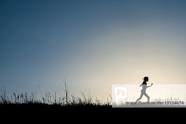 Silhouette girl running on grassy field against clear sky during dusk