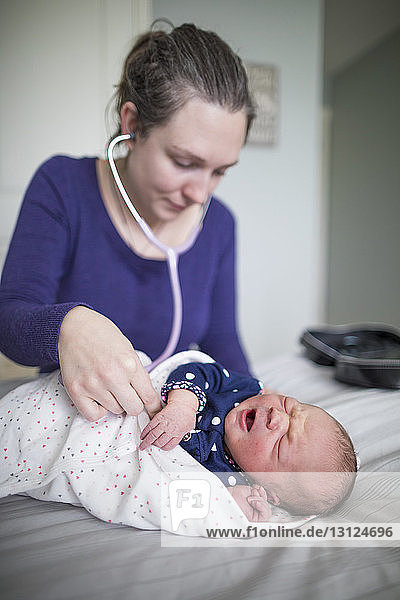 Hebamme untersucht neugeborenes Mädchen mit Stethoskop am Bett zu Hause