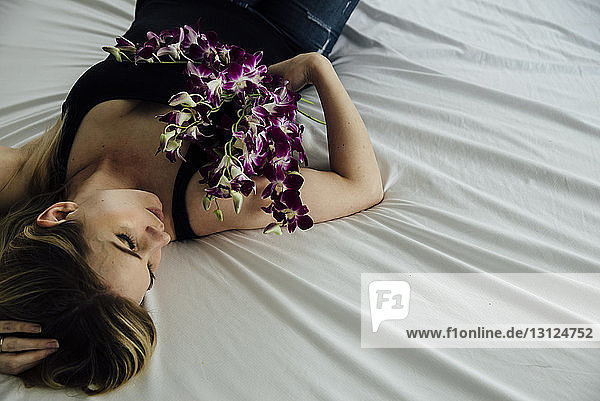 Hochwinkelaufnahme einer verführerischen Frau  die Blumen hält  während sie zu Hause auf dem Bett liegt