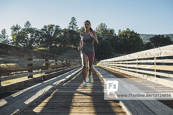Sportswoman running at wooden bridge on sunny day