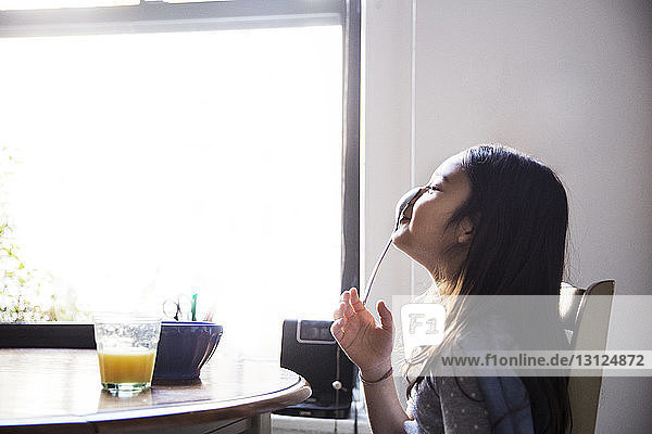 Seitenansicht eines Mädchens  das den Löffel auf der Nase balanciert  während es in der Küche am Tisch sitzt