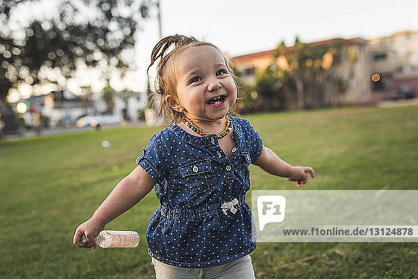 Glückliches kleines Mädchen schaut weg  während es auf einem Grasfeld gegen den Himmel im Park steht