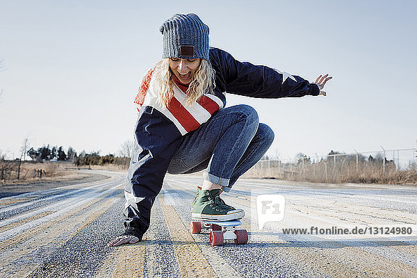 Verspielte Frau in voller Länge beim Skateboarden auf der Straße im Winter