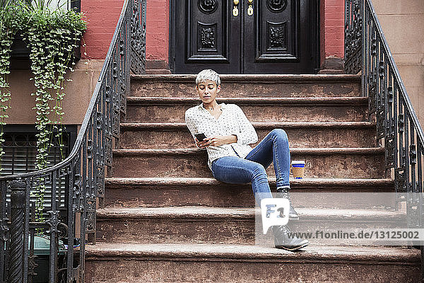 Frau benutzt Mobiltelefon  während sie auf Stufen sitzt