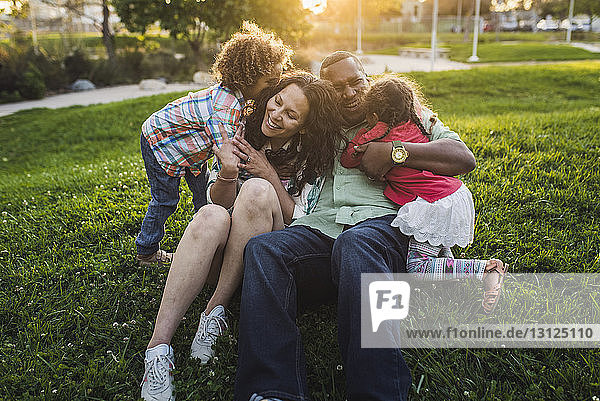 Children embracing parents on grassy field at park during sunset