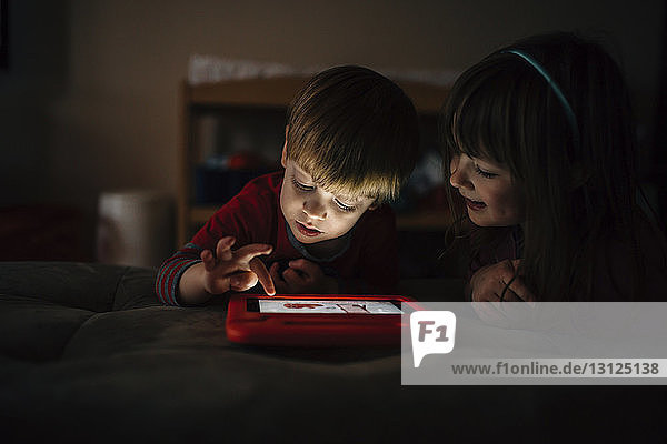 Glückliche Geschwister spielen Videospiel  während sie zu Hause im Bett liegen