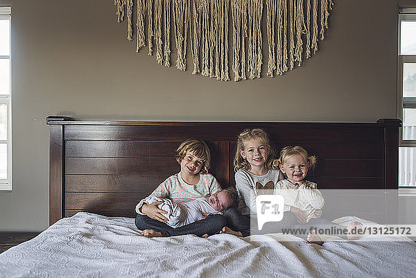 Portrait of smiling sisters with baby girl sitting on bed at home