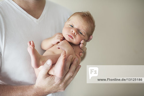 Midsection of father carrying newborn shirtless son against wall at home