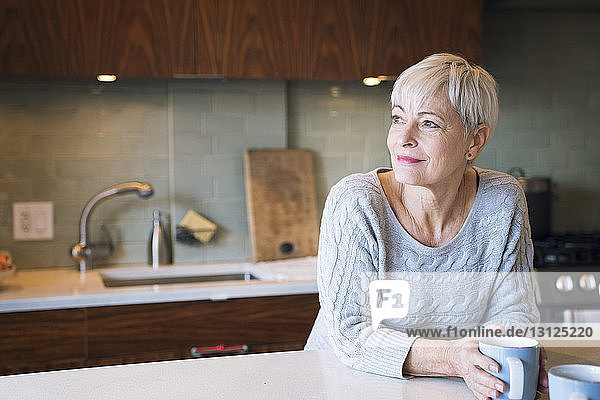 Thoughtful senior woman looking away while leaning on table