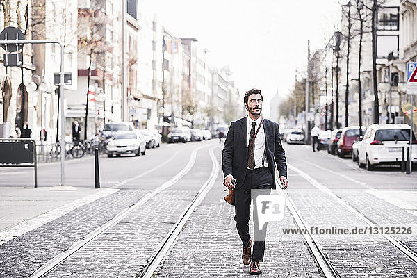 Full length of businessman walking by railroad tracks in city