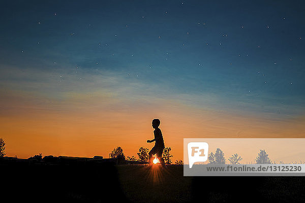 Silhouettenjunge geht bei Sonnenuntergang auf dem Feld gegen den Himmel