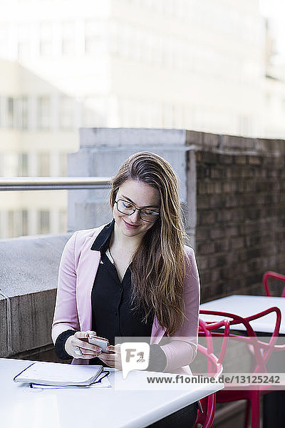 Geschäftsfrau benutzt Mobiltelefon  während sie auf dem Balkon sitzt