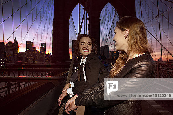 Fröhliche Freunde schauen sich an  während sie auf der Brooklyn Bridge stehen