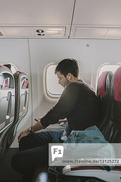 Seitenansicht eines Mannes bei der Benutzung eines Mobiltelefons während einer Reise im Flugzeug