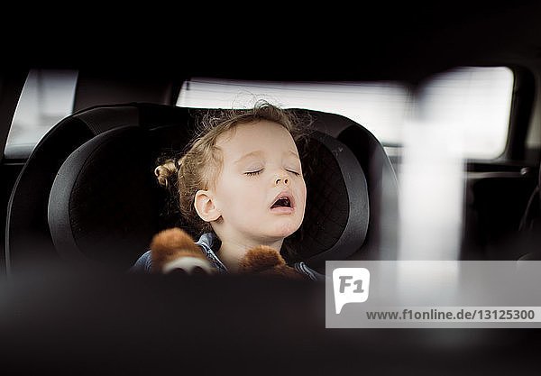 Cute girl with mouth open sleeping in car seen through vehicle seat